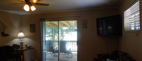 A living room with a ceiling fan, a television, a sofa, and a sliding glass door leading to an outdoor patio area.