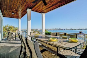 Un espacio de comedor al aire libre con techo de madera, pilares blancos y vistas al agua y al muelle.
