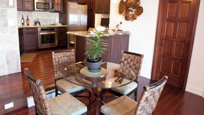 A modern kitchen with dark wood cabinets, stainless steel appliances, and a dining area with wicker chairs and a glass table. - Amazing Luxury ocean front Hamilton Cove Villa  w/electric cart (Avalon)