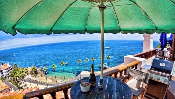 A balcony with a view of the ocean, a grill, and a table with a bottle. - Amazing Luxury ocean front Hamilton Cove Villa  w/electric cart (Avalon)