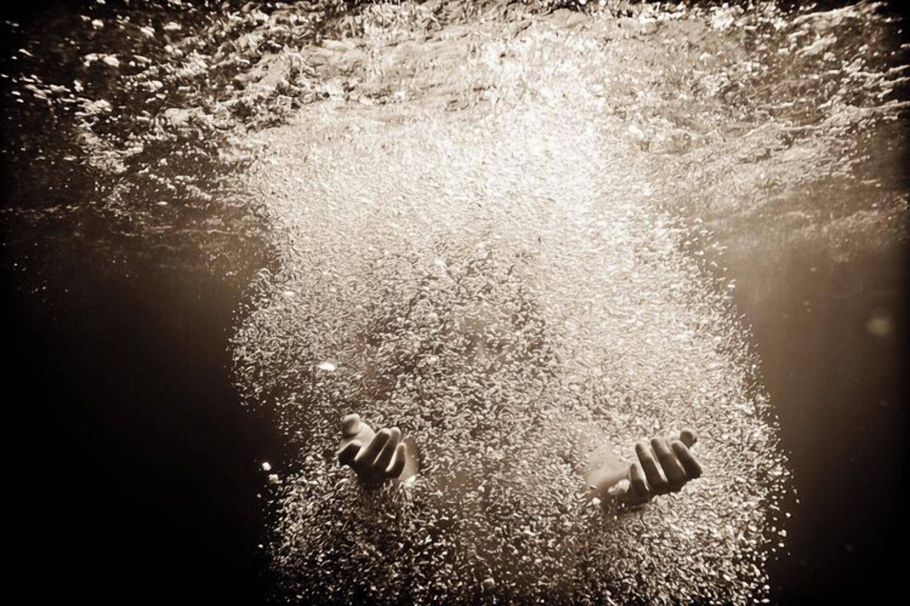 A person standing in a shallow body of water with sunlight reflecting off the surface.