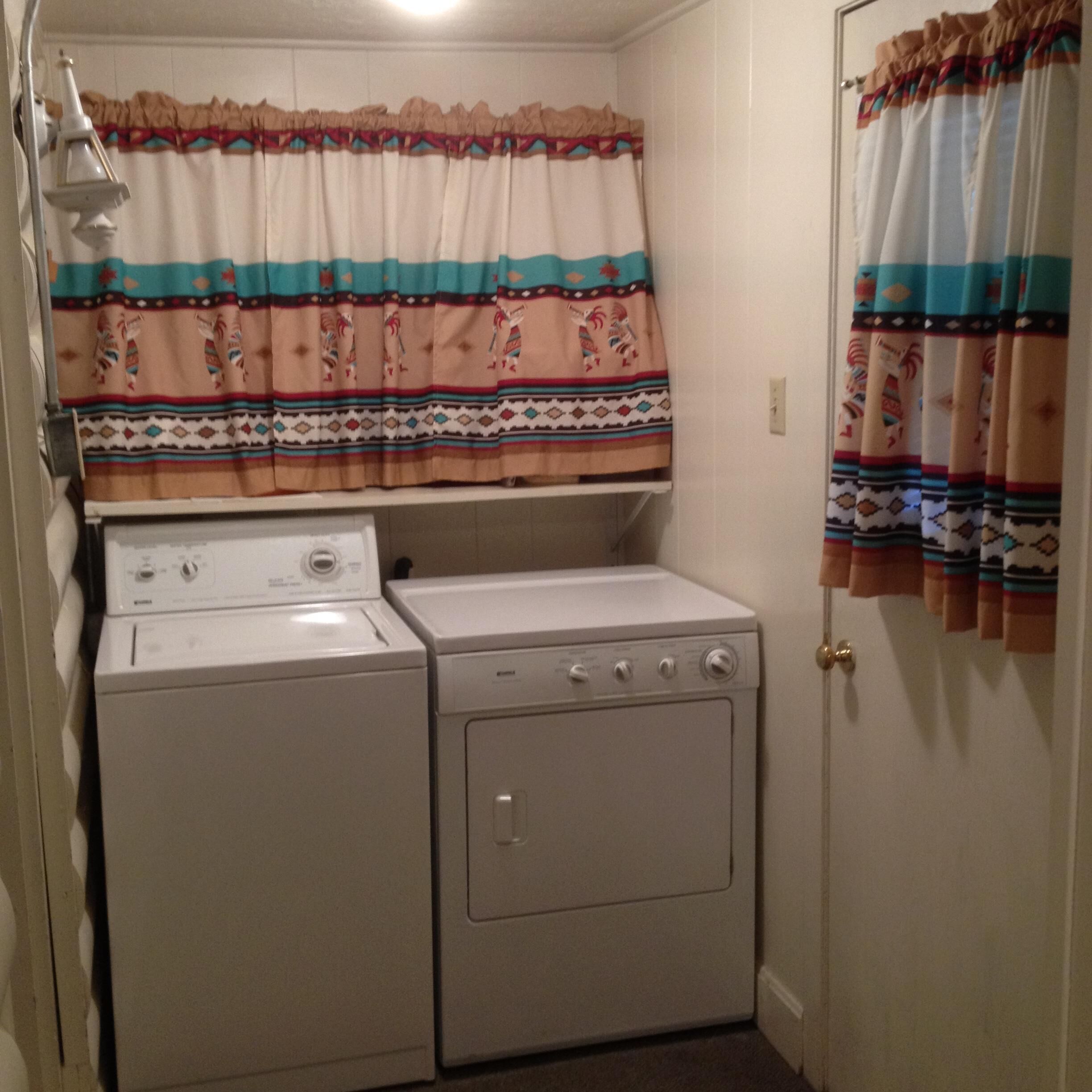 Une buanderie équipée de deux machines à laver et deux sèche-linge superposés, une fenêtre avec des rideaux à motifs et une porte avec des rideaux à rayures.