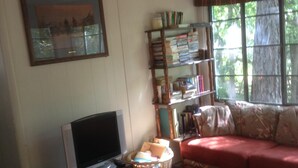 A living room with a television, bookshelf, and a sofa. - Relax at our River Front Cabin in Historic Upper Canyon  (Ruidoso)