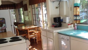 A kitchen with a stove, refrigerator, and dishwasher. There is a dining table with chairs and a window with curtains. - Relax at our River Front Cabin in Historic Upper Canyon  (Ruidoso)