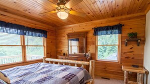 Un dormitorio de cabaña de madera con cama, cómoda, tocador y una mesita.
