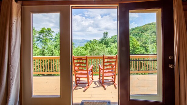 Una cabaña de madera con un amplio ventanal que da a una terraza con dos mecedoras.