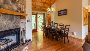 Comedor con chimenea de piedra, techo de madera y una mesa para cuatro personas.