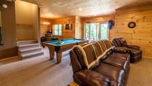 Una habitación acogedora con mesa de billar, sofá de cuero y una escalera que sube a otro nivel.