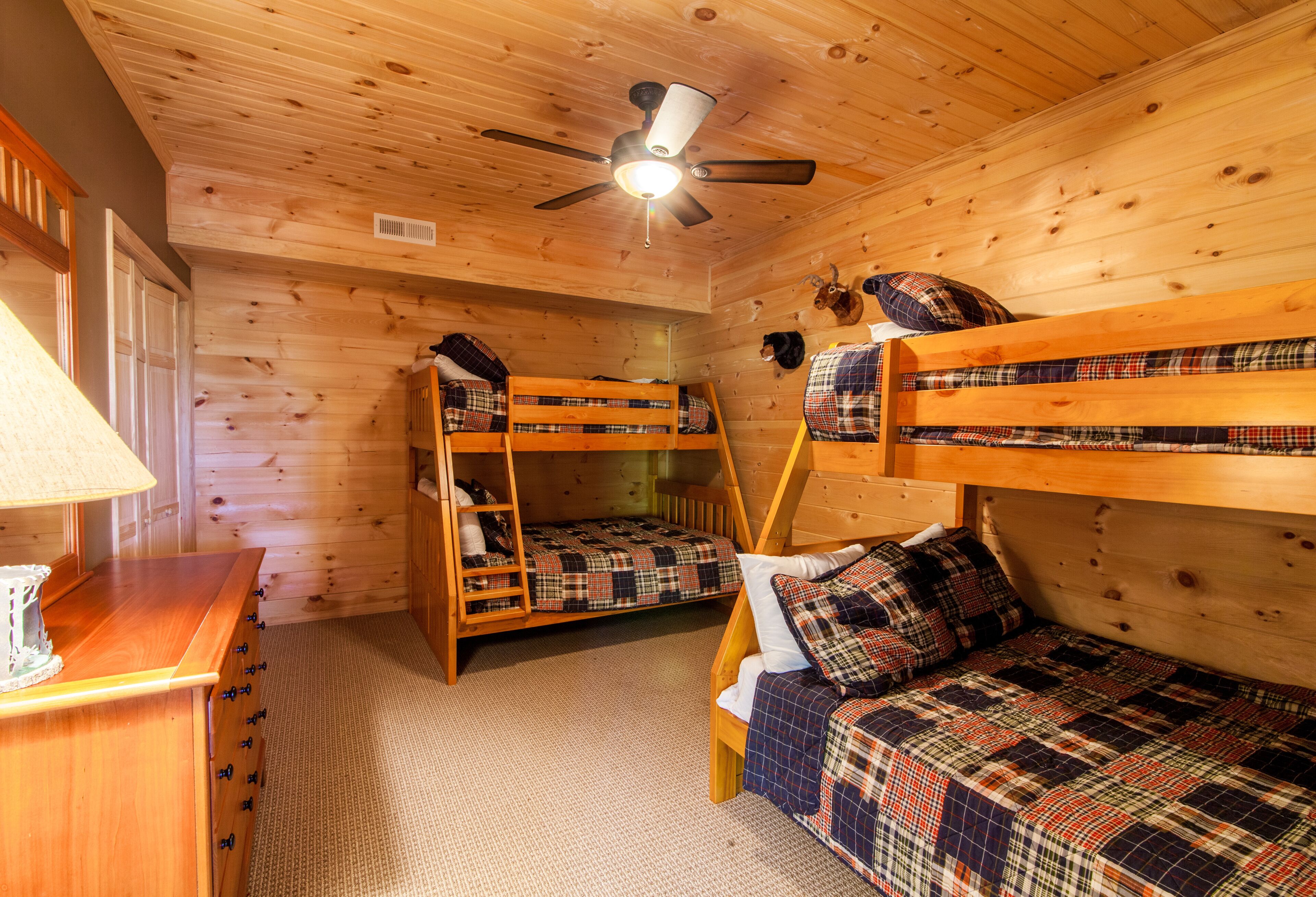 A wooden cabin room with bunk beds, a ceiling fan, and a wooden dresser.