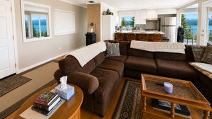 A living room with a brown sectional sofa, a coffee table, and a view of a kitchen and dining area.