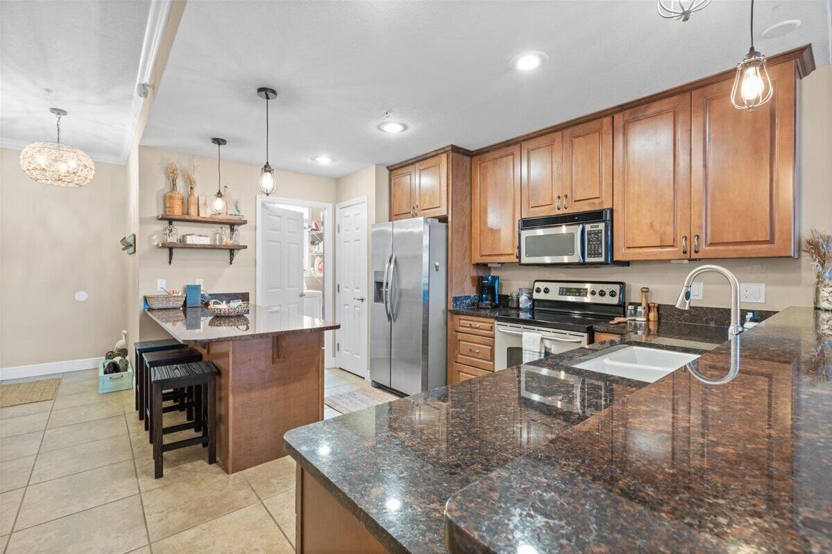 A modern kitchen with wooden cabinets, granite countertops, stainless steel appliances, and pendant lighting.