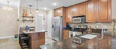 A modern kitchen with wooden cabinets, granite countertops, stainless steel appliances, and pendant lighting.