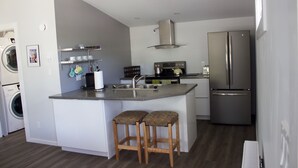 A modern kitchen with a built-in island, stainless steel appliances, and a washing machine in the adjacent laundry area. - Top loft garage suite close to Whyte Ave & University. Quick access to Downtown. (Edmonton)
