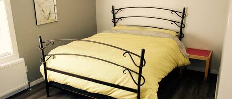 A bed with a metal frame, a yellow bedspread, and a wooden nightstand.