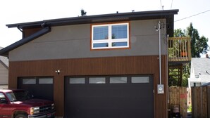 A modern two-story building with a garage, a red truck parked in front, and a wooden fence with a swing set. - Top loft garage suite close to Whyte Ave & University. Quick access to Downtown. (Edmonton)