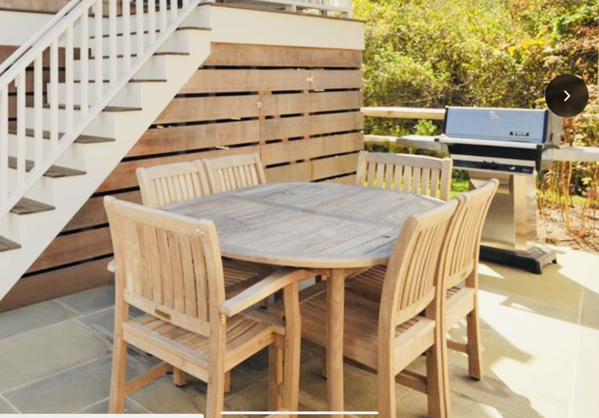 Une table à manger en bois, avec six chaises, un escalier et un barbecue dans un espace patio.