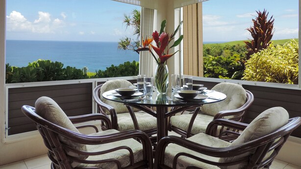 A dining area with a glass table and wicker chairs, overlooking a scenic ocean view. - AC!! Stunning Ocean Views - Walk to the beach #133-134 (Princeville)