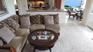 A living room with a sofa, coffee table, and a view of the kitchen and dining area. - AC!! Stunning Ocean Views - Walk to the beach #133-134 (Princeville)