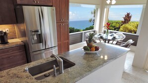 A kitchen with a stainless steel refrigerator, granite countertop, and a bowl of fruit. - AC!! Stunning Ocean Views - Walk to the beach #133-134 (Princeville)
