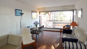 Una sala de estar con sofá, sillón, mesa de comedor y sillas. Hay un ventanal con vistas al exterior.