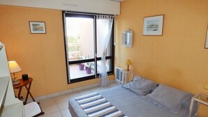 Habitación de hotel con cama, escritorio, silla, ventana con cortinas y una mesita de noche con lámpara.