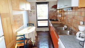 Una cocina compacta con armarios de madera, una mesa de comedor con sillas, una lámpara colgante y vistas a un espacio exterior por una puerta.