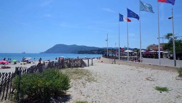 Una playa con banderas, una zona arenosa y una montaña a lo lejos.