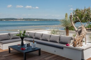 A terrace with a sofa and a table, overlooking a beach and the sea.