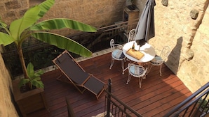 Una terraza de madera con una mesa, sillas, una tumbona y una planta en maceta.