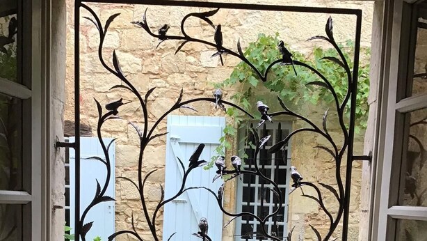 Una ventana con un marco metálico decorativo con pájaros y hojas.