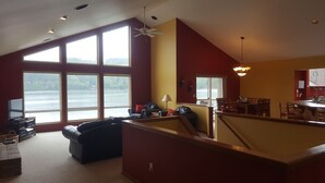 A spacious living area with a large window overlooking a body of water, a dining area with wooden furniture, and a kitchen with a bar counter. - Bobbi's Beach House is a spacious waterfront home with something for everyone! (Mount Vernon)