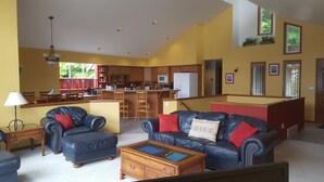 A living room with a black leather sofa, a wooden coffee table, and a kitchen in the background. - Bobbi's Beach House is a spacious waterfront home with something for everyone! (Mount Vernon)
