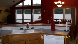 A kitchen with a large window overlooking a lake, a dishwasher, and a dining area with a table and chairs. - Bobbi's Beach House is a spacious waterfront home with something for everyone! (Mount Vernon)