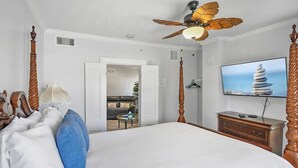 A hotel room with a large bed, a ceiling fan, a television, and a view of the outdoor seating area.