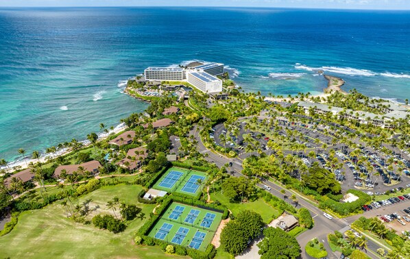 Vista aérea de un resort con varias canchas de tenis, un hotel grande y un estacionamiento.