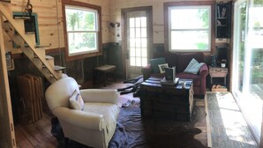 L’intérieur d’une cabane est agrémenté d’un escalier en bois, d’un fauteuil blanc, d’un canapé rouge et d’une grande fenêtre offrant une vue sur l’extérieur.