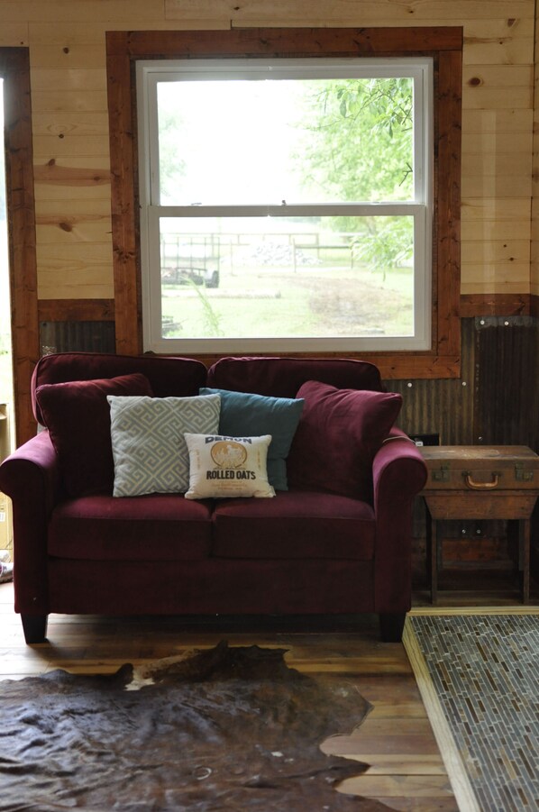Una habitación con interior de madera, un ventanal grande, un sofá rojo con cojines estampados y una maleta.