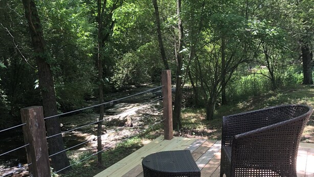 Une terrasse en bois, meublée de meubles en osier, entourée d’une végétation luxuriante et d’arbres.