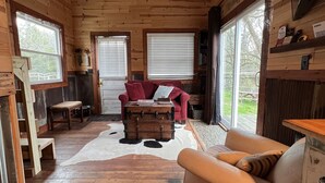 L’intérieur d’une cabane avec des murs en bois, un ventilateur de plafond, un canapé rouge, un canapé blanc, une table basse en bois et un tapis en peau de vache.