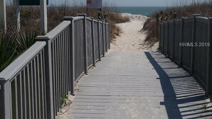A wooden boardwalk leading to a sandy beach area, flanked by metal railings.