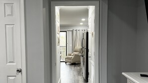 A hallway with a wooden floor, white walls, and a door on the left.