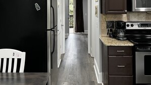 A kitchen with a black refrigerator, a microwave, and a stove. There is a fish decoration on the refrigerator. The kitchen has wooden flooring and dark brown cabinets.