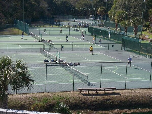 A tennis court with multiple players, benches, and a fence.