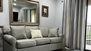 A modern living room with a grey sofa, a large mirror, and a window with curtains.