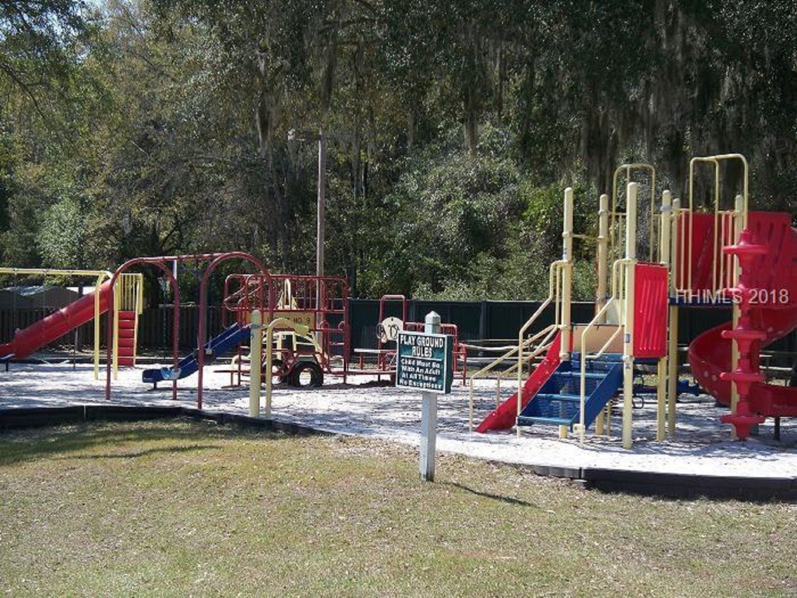 A playground with various play structures including slides and climbing frames, surrounded by trees.
