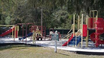 A playground with various play structures including slides and climbing frames, surrounded by trees.