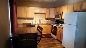 A compact kitchen with wooden cabinets, a microwave, a stove, and a refrigerator. - SADDLE MOUNTAIN ESCAPE (Clancy)