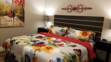 Une chambre à coucher avec une couvre-lit à motifs floraux, une table de chevet avec une lampe et un élément décoratif fixé au mur.