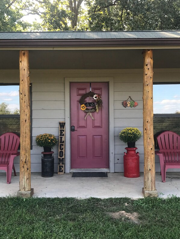 Une véranda en bois avec une porte violette, deux plantes en pot et deux chaises rouges.