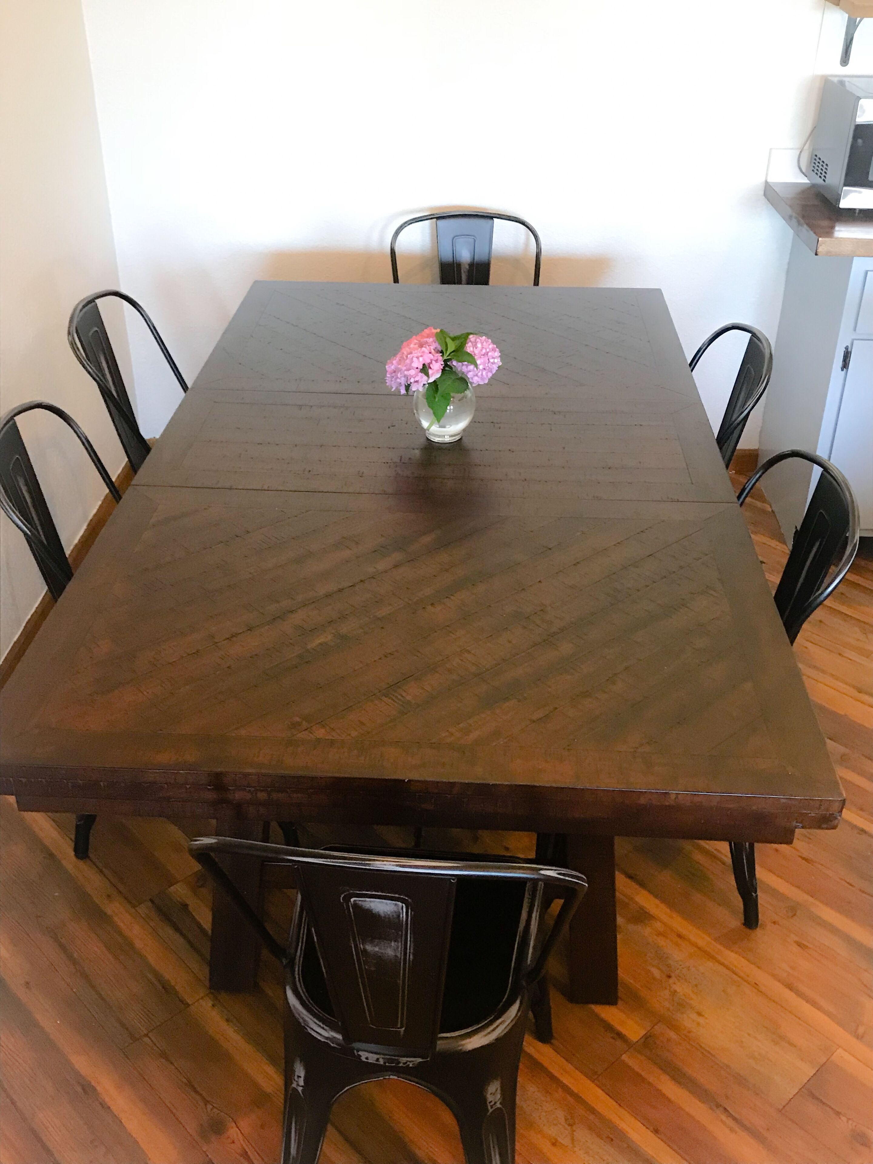 A rectangular wooden dining table with a vase of flowers in the center, surrounded by six chairs.